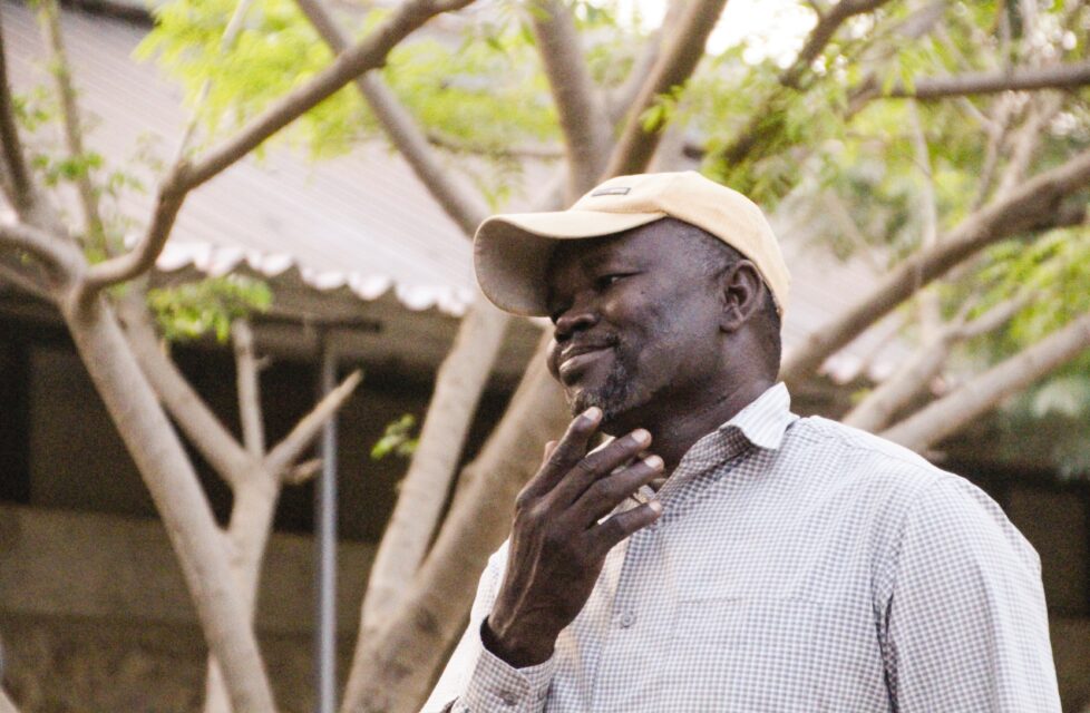 Sudanese Pastor in Nuba Mountains Serves Imprisoned Muslims a man stands outside his home smiling