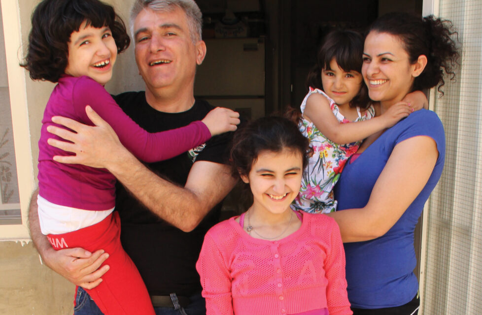 ISIS Fighters Destroy Assyrian Christian Villages, Burn Churches a husband and wife stand with their three girls outside their house smiling